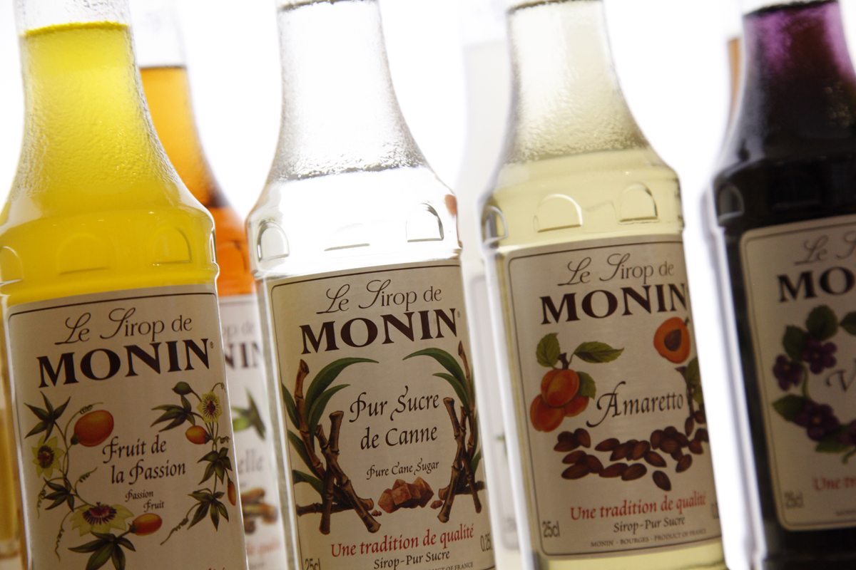 Bouteille de sirop Monin posée sur un comptoir, à côté d'un verre de boisson fraîche