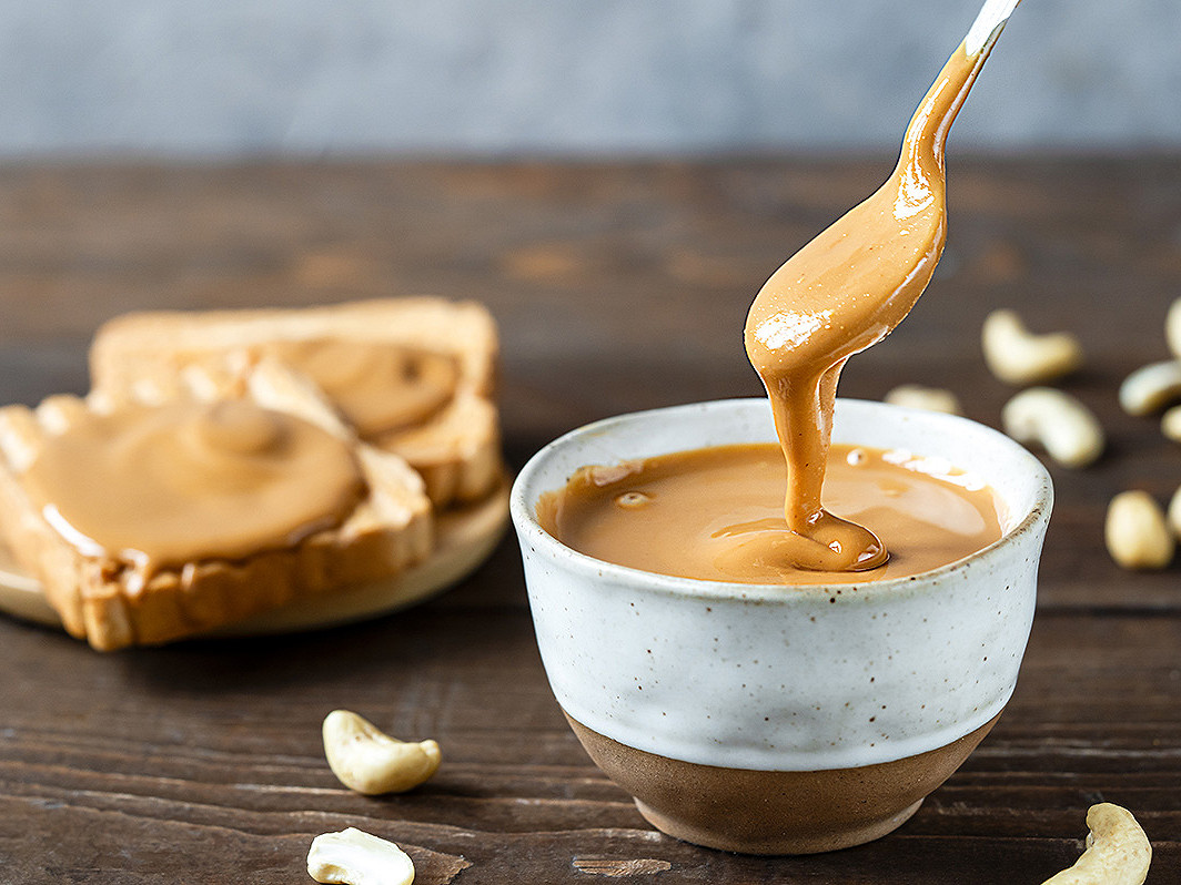 Pot de peanut butter crémeux avec une cuillère et des cacahuètes