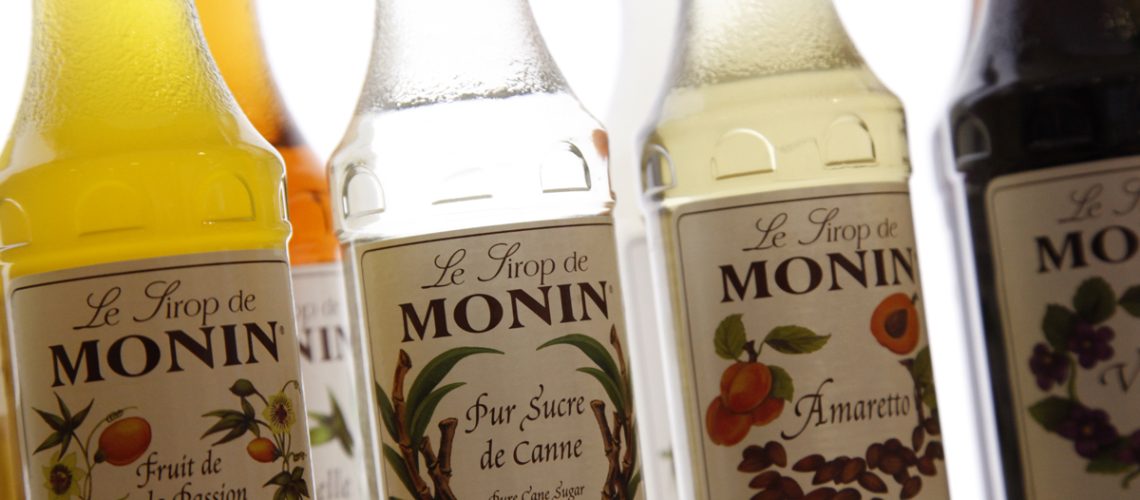Bouteille de sirop Monin posée sur un comptoir, à côté d'un verre de boisson fraîche