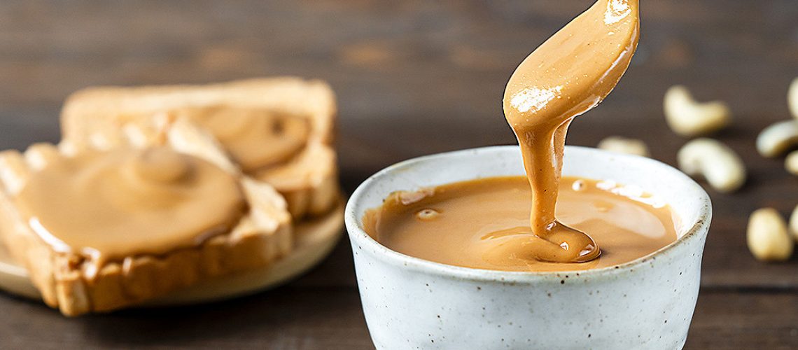 Pot de peanut butter crémeux avec une cuillère et des cacahuètes